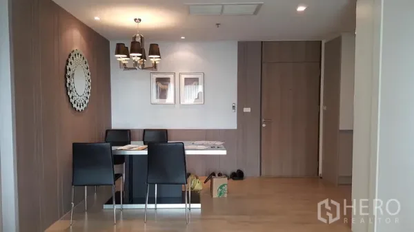 Condominium for rent in Khlong Toei, Bangkok - Dining area with four black chairs, wall mirror and stylish pendant lights.