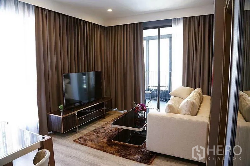 公寓 出租在Huai Khwang, Bangkok - 明亮的公寓客厅，米色沙发、电视柜，推拉门通向阳台。