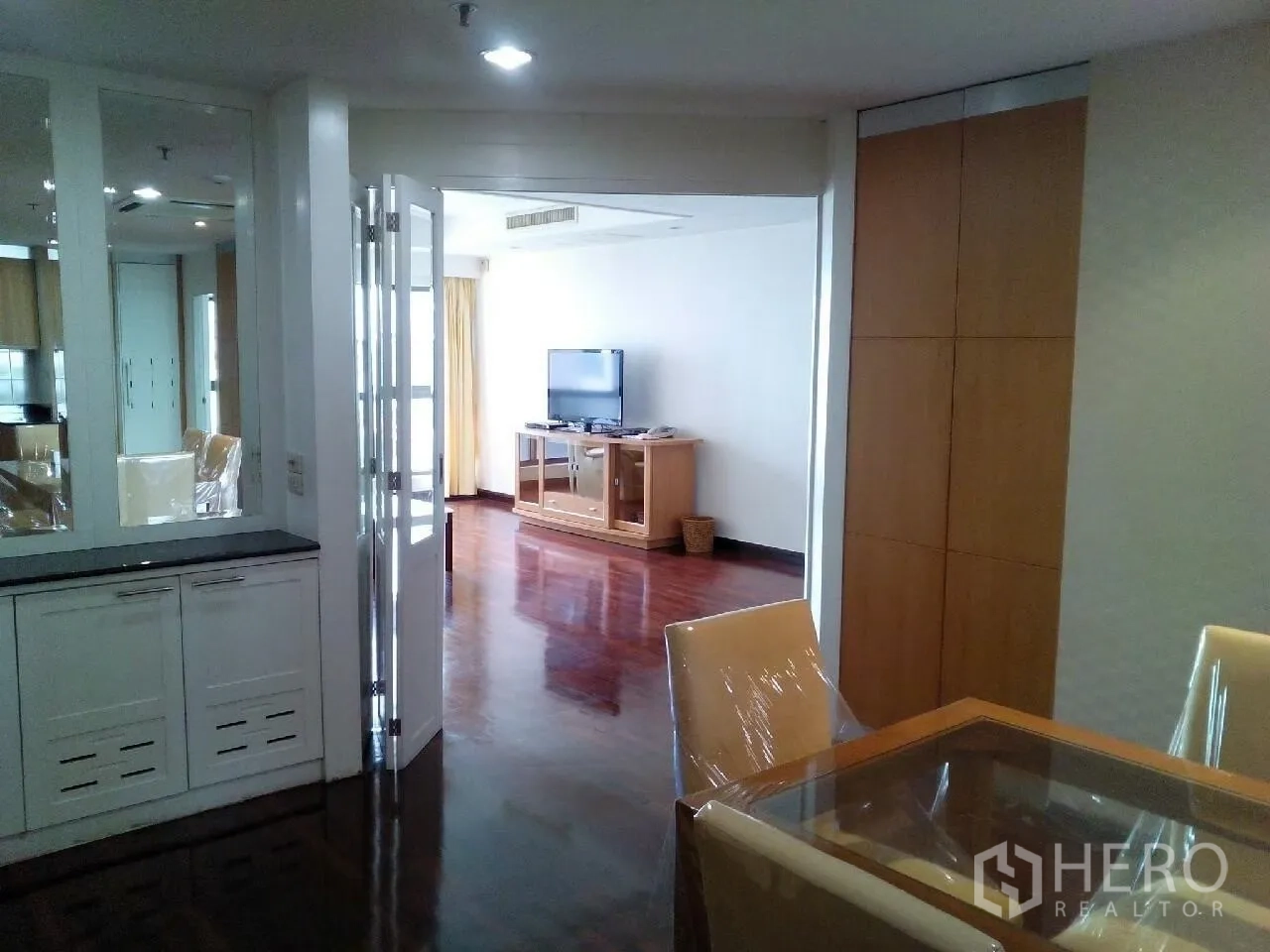 Condominium for rent in Phaya Thai, Bangkok - Dining nook with glass-top table and chairs beside mirrored built-in cabinetry and folding doors to the lounge.