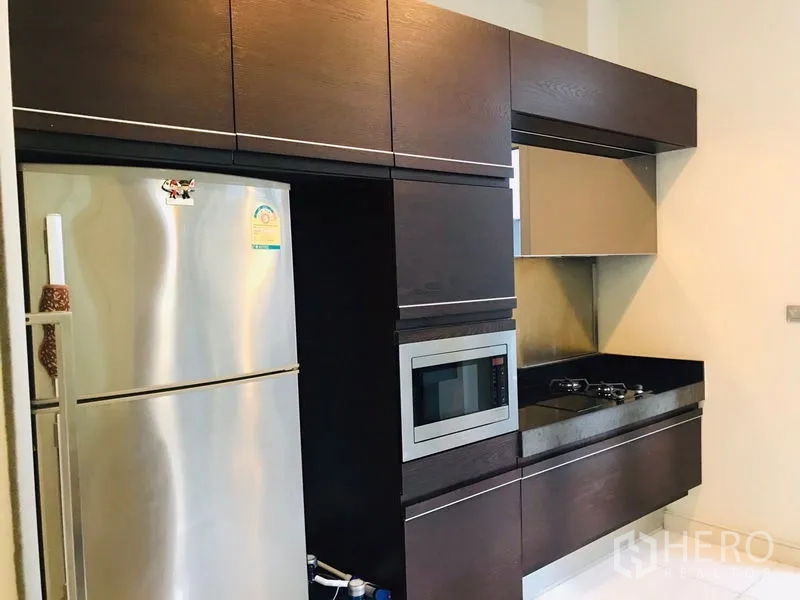 Townhouse for rent or sale in Chatuchak, Bangkok - Modern kitchen with dark cabinetry, gas hob, stainless refrigerator and microwave.