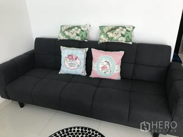 Condominium for rent in Bang Lamung, Chon Buri - Compact dark fabric sofa with patterned cushions against a clean white wall.