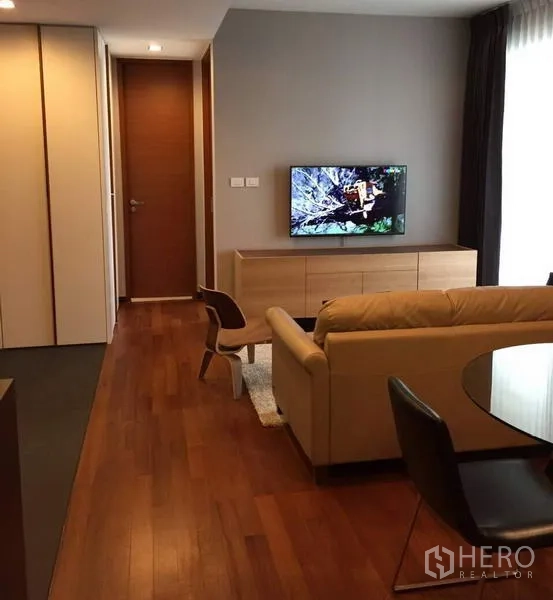 Condominium for rent in Khlong Toei, Bangkok - Open-plan living area with sofa, wooden TV console, round dining table and warm hardwood floors.