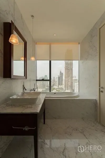 Condominium for rent in Watthana, Bangkok - Marble bathroom with vanity and bathtub set beneath a large window framing Bangkok city views.