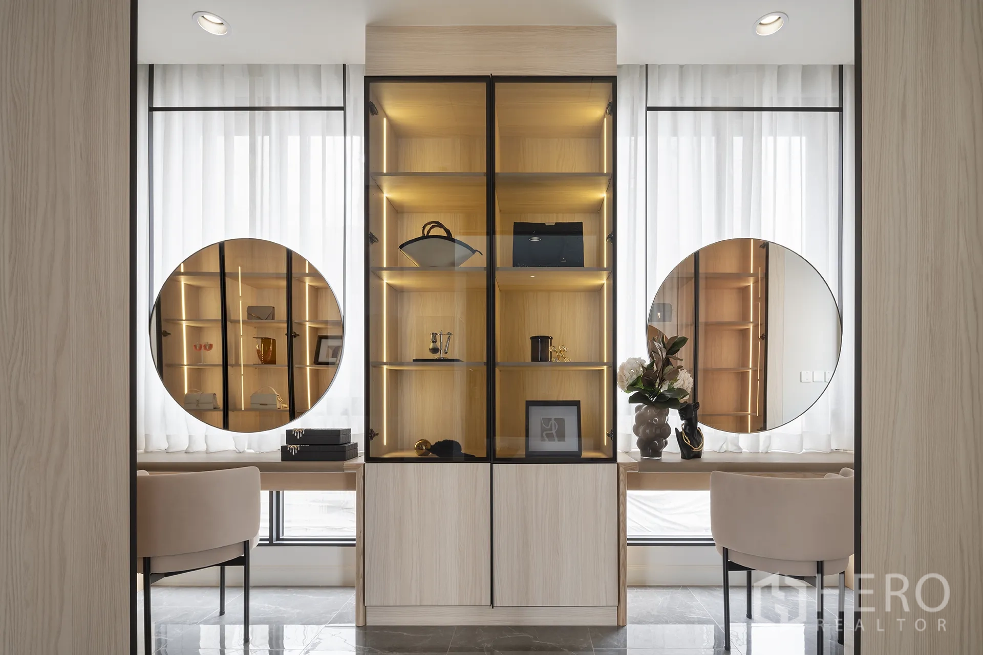 Detached House for sale in Yan Nawa, Bangkok - Illuminated glass display cabinet flanked by round mirrors, built-in desks and upholstered chairs beside tall sheer-draped windows.