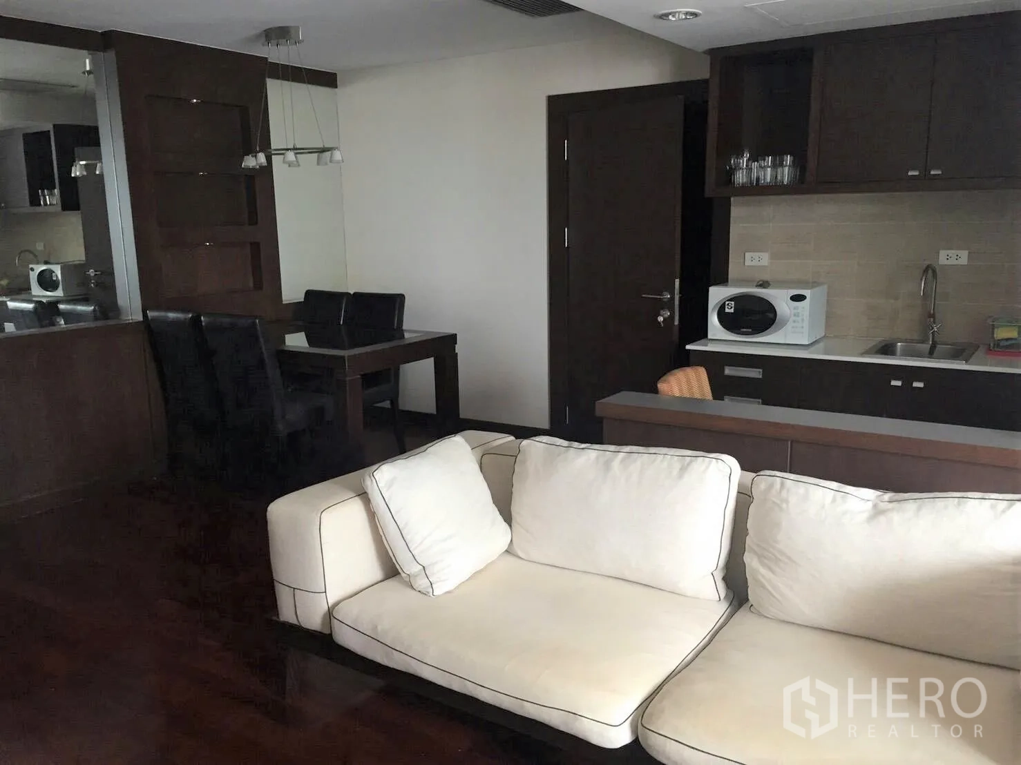 公寓 出租在Pathum Wan, Bangkok - 开放式客餐厅，米色沙发与深色橱柜的紧凑厨房