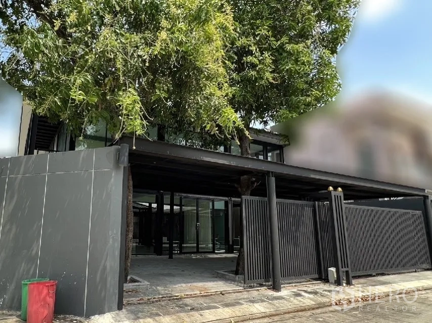 Detached House for rent or sale in Phra Khanong, Bangkok - Corner view of gated entrance and large covered carport shaded by a mature tree.