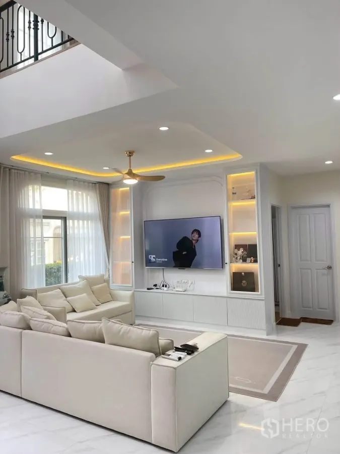 Detached House for rent or sale in Bang Phli, Samut Prakan - Living room with L-shaped sofa, built-in illuminated shelves and wall-mounted TV.