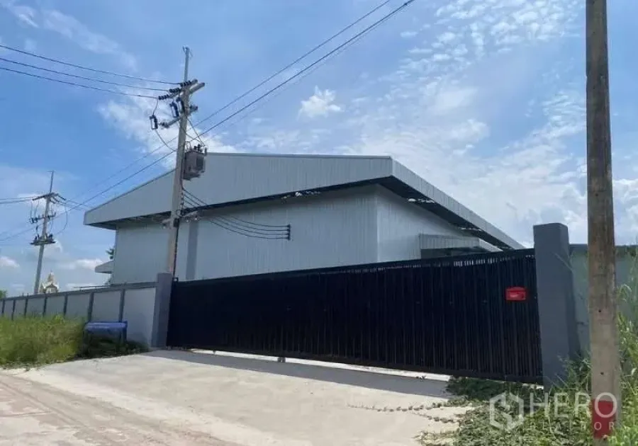 货栈 出售在Ban Bueng, Chon Buri - 金属外墙仓库外观，黑色滑动大门与围墙，可见电线，位于春武里Ban Bueng。