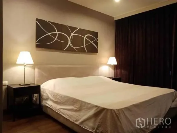 公寓 出租在Sathon, Bangkok - 主卧配大床、床头灯、抽象装饰画与遮光窗帘。