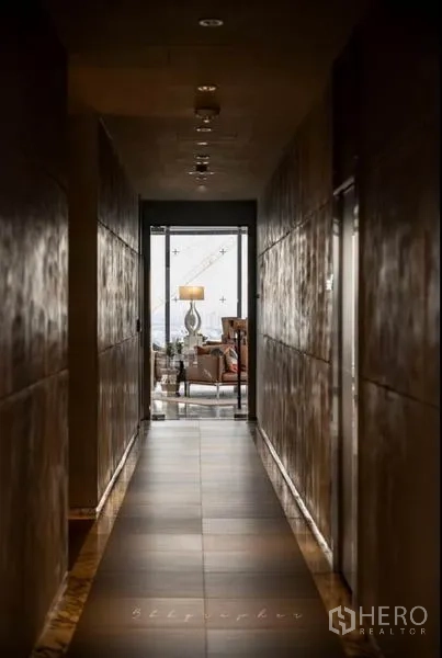 Condominium for rent or sale in Watthana, Bangkok - Dim hallway leading to a bright lounge with a floor lamp and city views.