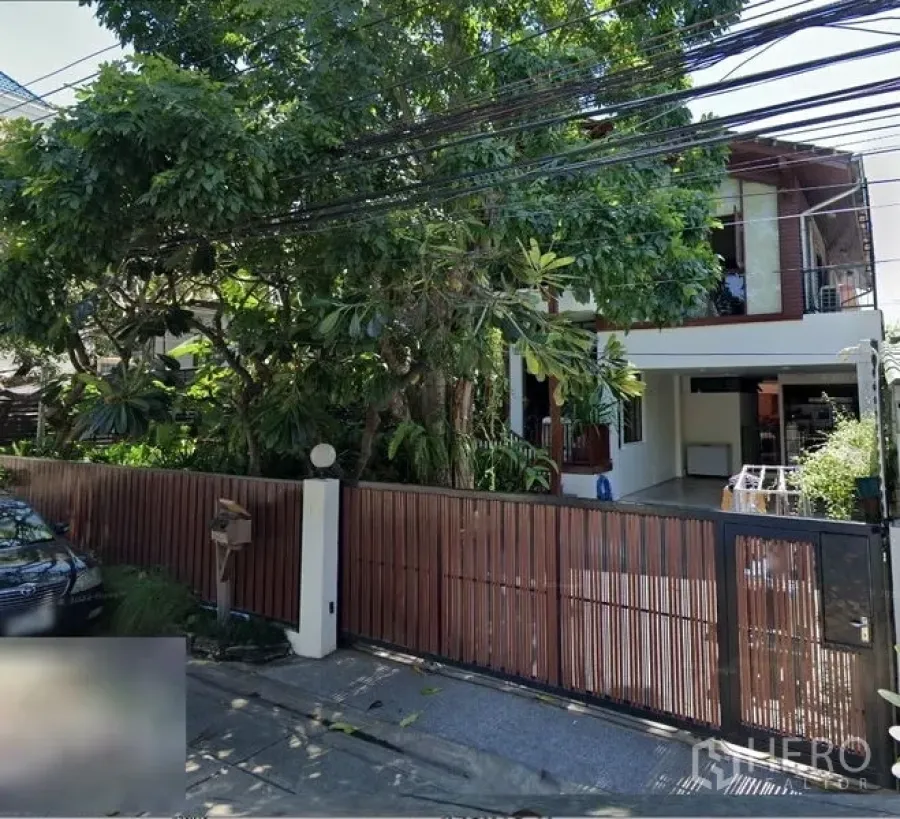 Detached House for sale in Suan Luang, Bangkok - Gated entrance with wooden fence, carport and mature shade trees along the street.