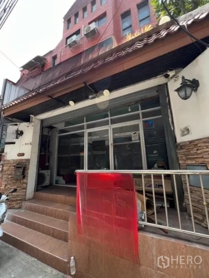 带办公室的家 出租在Watthana, Bangkok - 通罗联排住办合一外观，宽玻璃门面与红色瓦檐的街景斜拍。