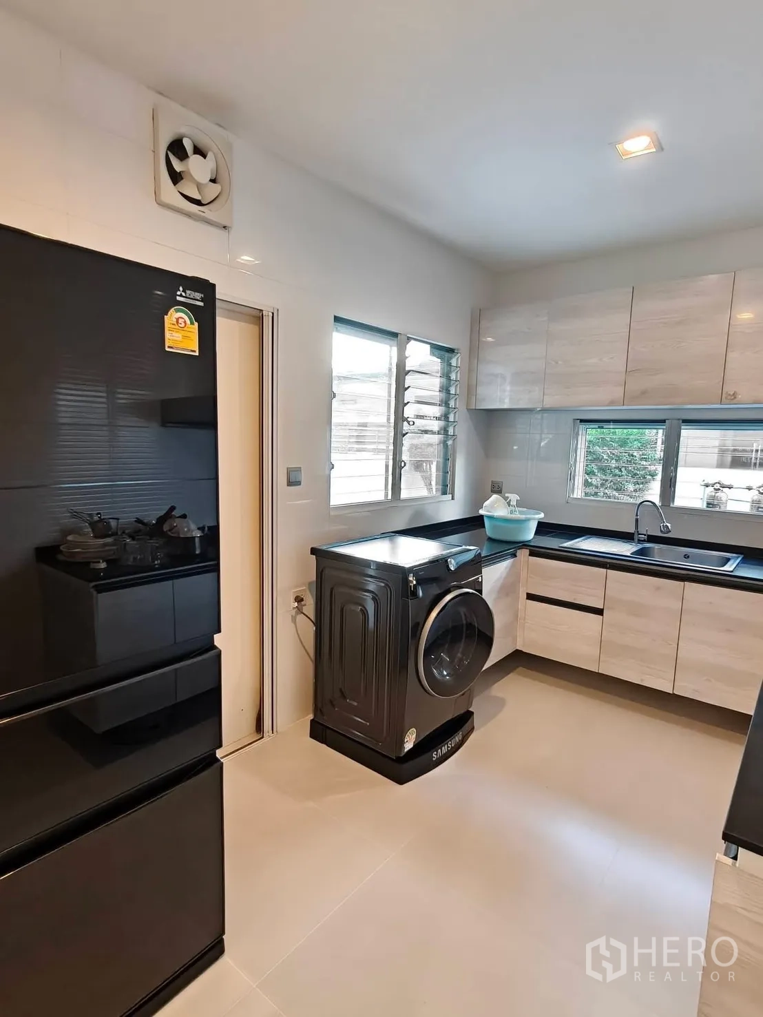 บ้านเดี่ยว for rent or sale in Bang Phli, Samut Prakan - ครัวแยกสไตล์โมเดิร์นพร้อมตู้เย็นสีดำ ตู้เก็บของ และเครื่องซักผ้า.