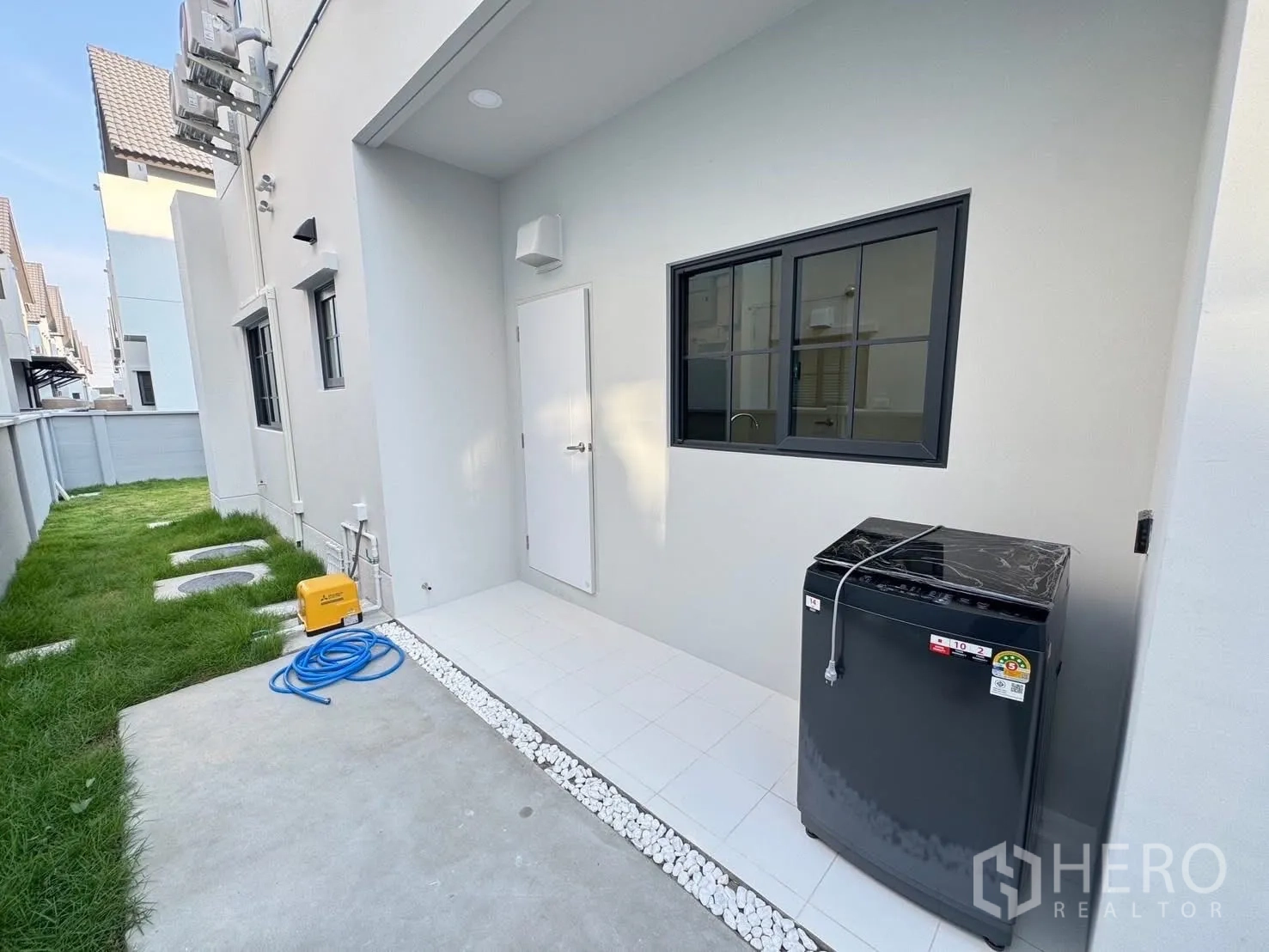 บ้าน for rent in Bang Phli, Samut Prakan - พื้นที่ซักล้างภายนอก มีเครื่องซักผ้า พื้นกระเบื้อง และทางเดินหญ้าริมกำแพง