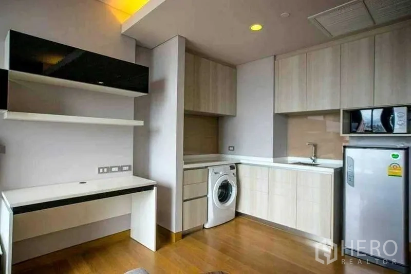 Condominium for rent in Khlong Toei, Bangkok - Compact L-shaped kitchen with cabinets, sink, fridge and washing machine.