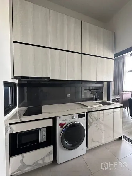Condominium for rent in Phra Khanong, Bangkok - Modern kitchenette with marble-look cabinetry, built-in microwave and front-load washer.