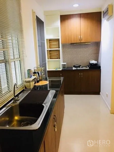 Townhouse for rent in Bang Kapi, Bangkok - Modern galley kitchen with upper cabinets, cooktop and black stone counters.