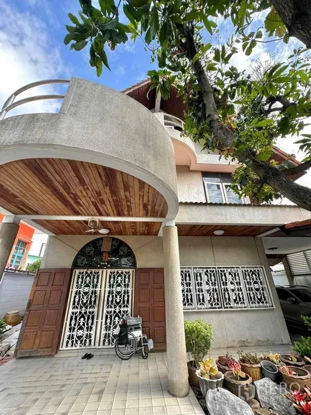 Detached House for sale in Yan Nawa, Bangkok - Facade with curved balcony, wood-clad carport ceiling and secure iron-grille windows.