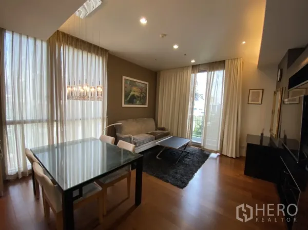 公寓 出租在Watthana, Bangkok - 明亮的客餐厅，落地窗帘、玻璃餐桌、沙发并可通往阳台。