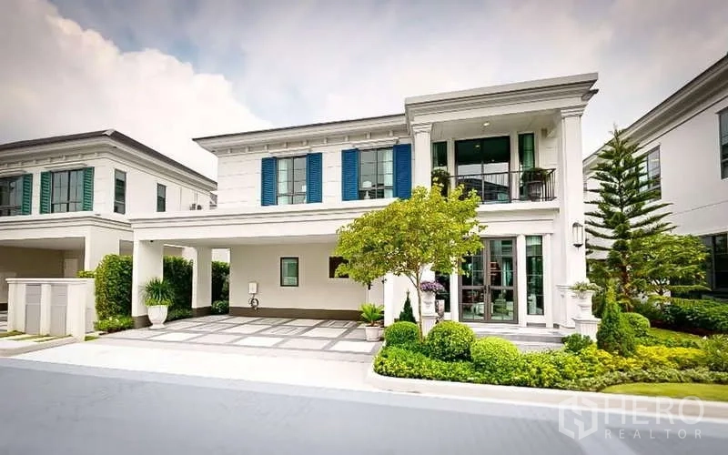 独立式住宅 出租在Bang Phli, Samut Prakan - 优雅的两层独栋别墅外观，带车棚，蓝色百叶窗与修剪整齐的绿化。