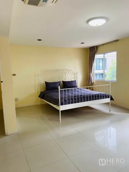 Detached House for rent in Watthana, Bangkok - Spacious bedroom with metal bedframe, corner windows and tiled floors.