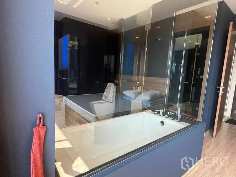 Condominium for sale in Phaya Thai, Bangkok - Glass‑partitioned bathroom showing bathtub and toilet from the bedroom side.