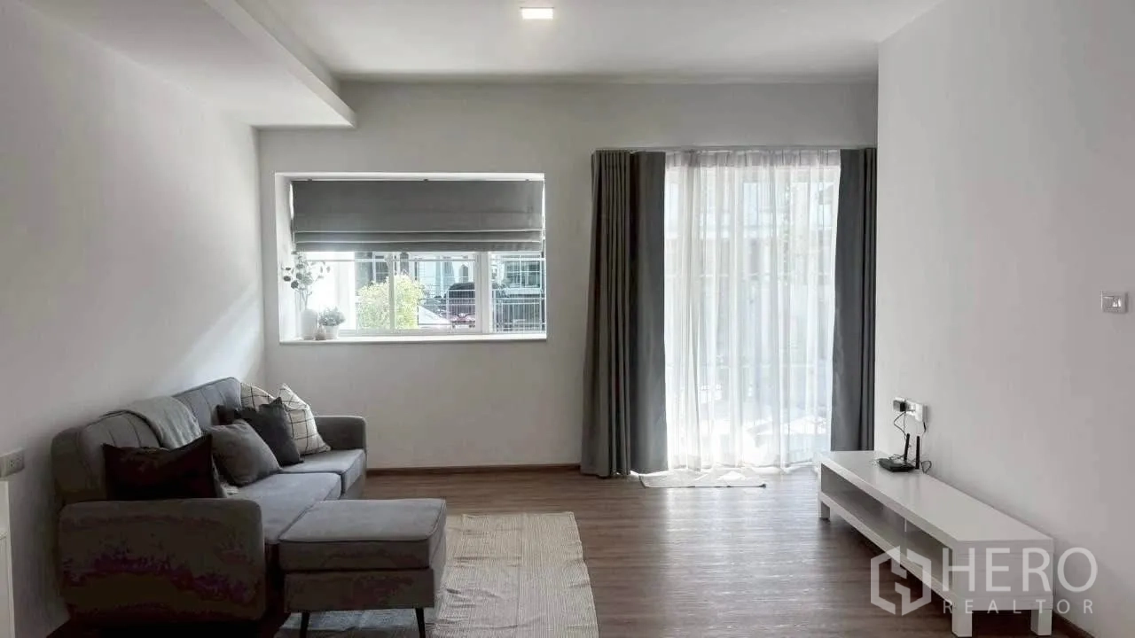 联排别墅 for rent in Prawet, Bangkok - 明亮客厅，转角沙发、电视柜与通往露台的推拉玻璃门。
