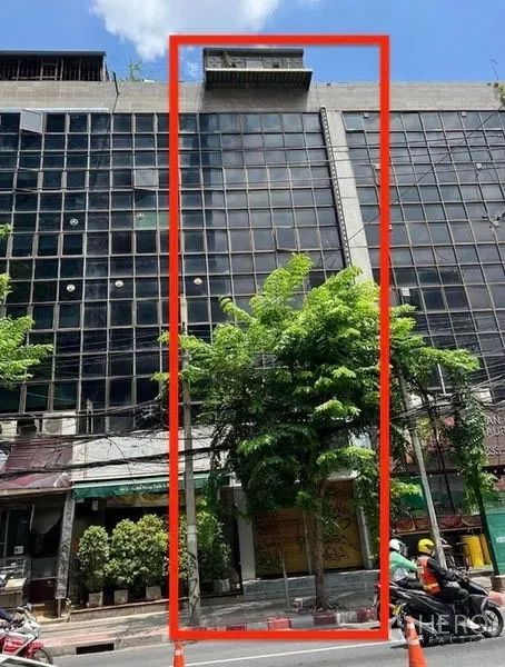 Shophouse for rent in Bang Rak, Bangkok - Narrow glass-front commercial building in a row of offices on a busy Bangkok street with greenery and overhead cables.