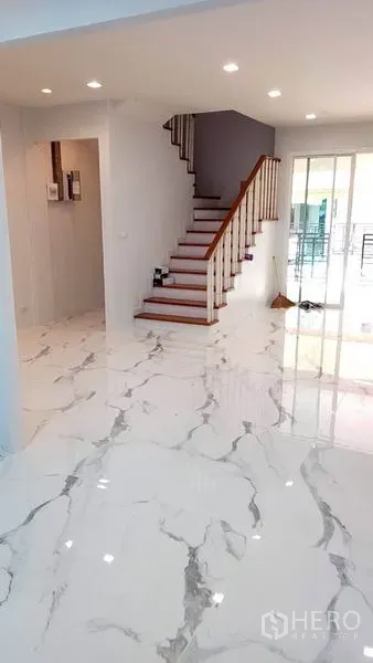 Townhouse for rent in Yan Nawa, Bangkok - Spacious living room with glossy tiles and a wooden staircase.