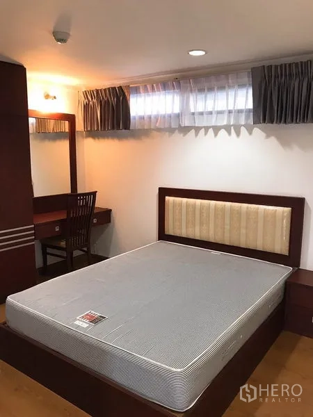 Condominium for rent or sale in Watthana, Bangkok - Cozy bedroom with upholstered headboard, mattress, wood dressing table and curtained windows.