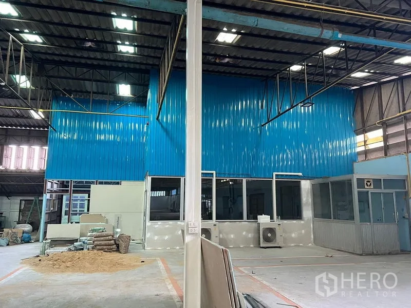 Warehouse for rent in Samut Prakan - High-ceiling warehouse interior with blue metal partition, glass-front offices and an AC unit.