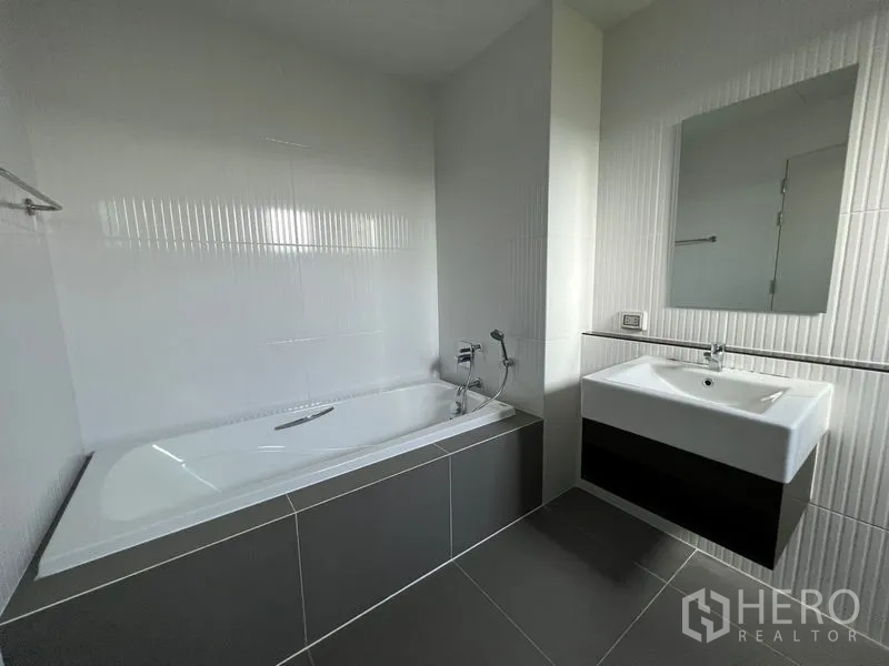 Detached House for rent in Saphan Sung, Bangkok - Bathroom with built-in bathtub, vanity and wall mirror in monochrome tones.