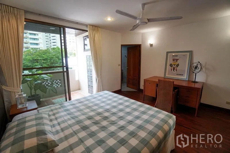 Apartment for rent in Watthana, Bangkok - Bedroom with desk, balcony access, ceiling fan, and an entrance to the en-suite bathroom.