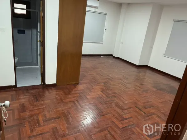 Detached House for rent in Watthana, Bangkok - Large room with parquet wood flooring, white walls and a doorway to an ensuite bathroom.