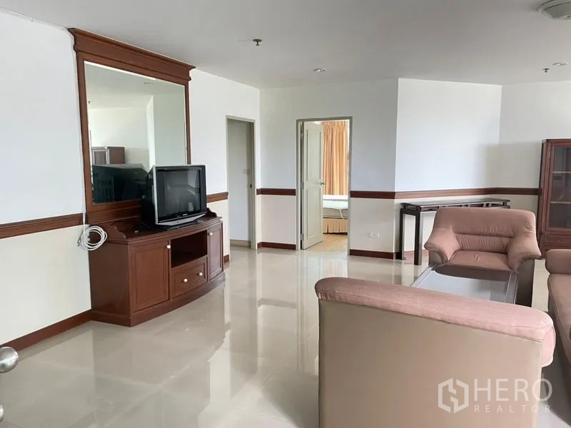 Condominium for rent in Khlong Toei, Bangkok - Living area featuring TV cabinet, large wall mirror, and glossy tile flooring.