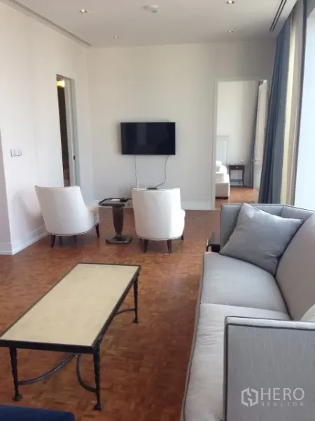 Condominium for rent or sale in Bang Rak, Bangkok - Bright living room with sofa, armchairs and TV facing floor-to-ceiling windows in a Bang Rak high-rise condo.