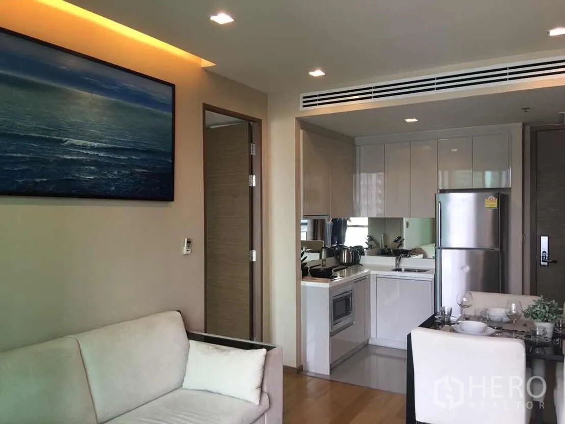 Condominium for rent or sale in Bang Rak, Bangkok - Open-plan living room with sofa, compact white kitchen and small dining nook