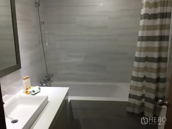 คอนโด ให้เช่าในWatthana, Bangkok - ห้องน้ำสมัยใหม่พร้อมอ่างอาบน้ำและฝักบัว ผ้าม่านลายทาง เคาน์เตอร์ซิงก์สีขาวและกระจกบานใหญ่