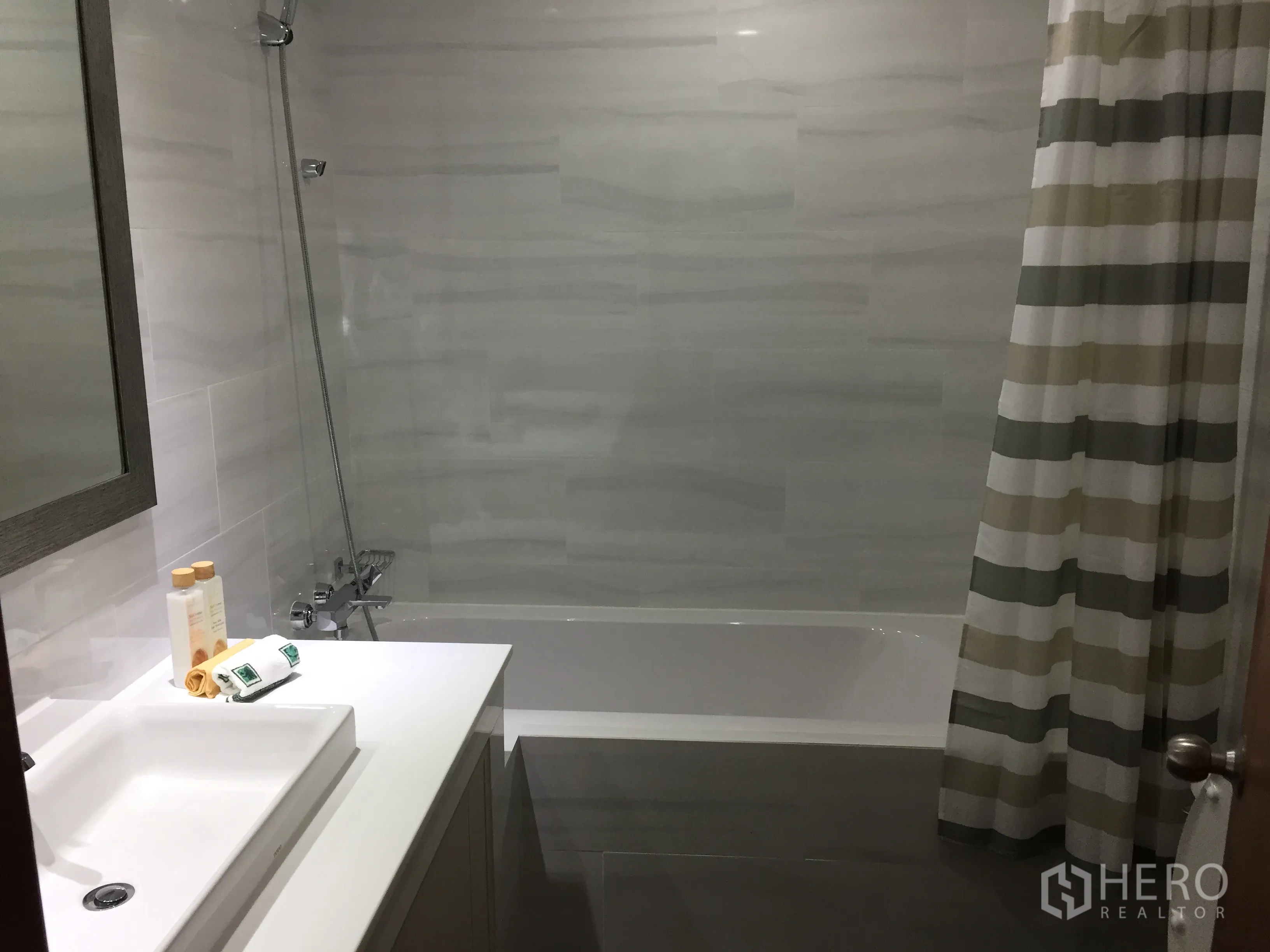 คอนโด ให้เช่าในWatthana, Bangkok - ห้องน้ำสมัยใหม่พร้อมอ่างอาบน้ำและฝักบัว ผ้าม่านลายทาง เคาน์เตอร์ซิงก์สีขาวและกระจกบานใหญ่