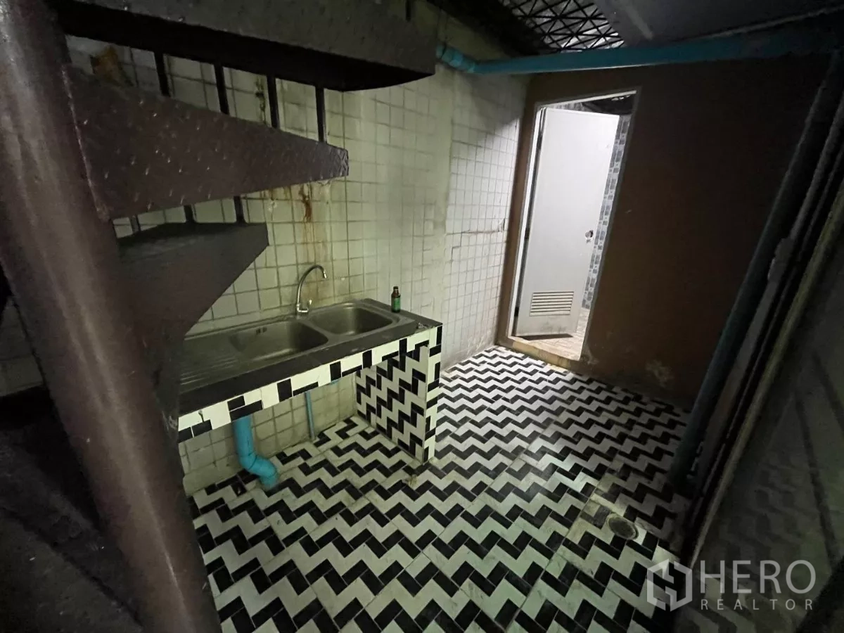 Shophouse for rent in Watthana, Bangkok - Utility zone with a double stainless-steel sink, herringbone tiles and a spiral staircase next to a bathroom door.