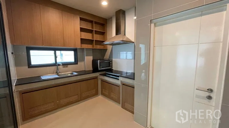 Detached House for rent in Bang Kapi, Bangkok - Fitted kitchen with wooden cabinets, black countertop, range hood and a window.