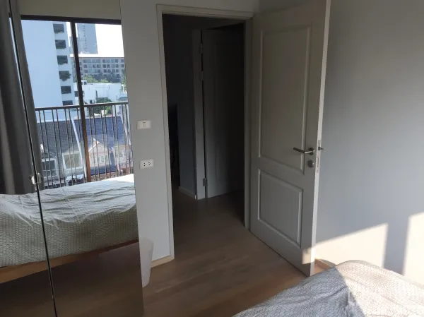 Condominium for rent in Bangkok - Bedroom with light wood floors, open door to hallway, and a large window to a balcony.