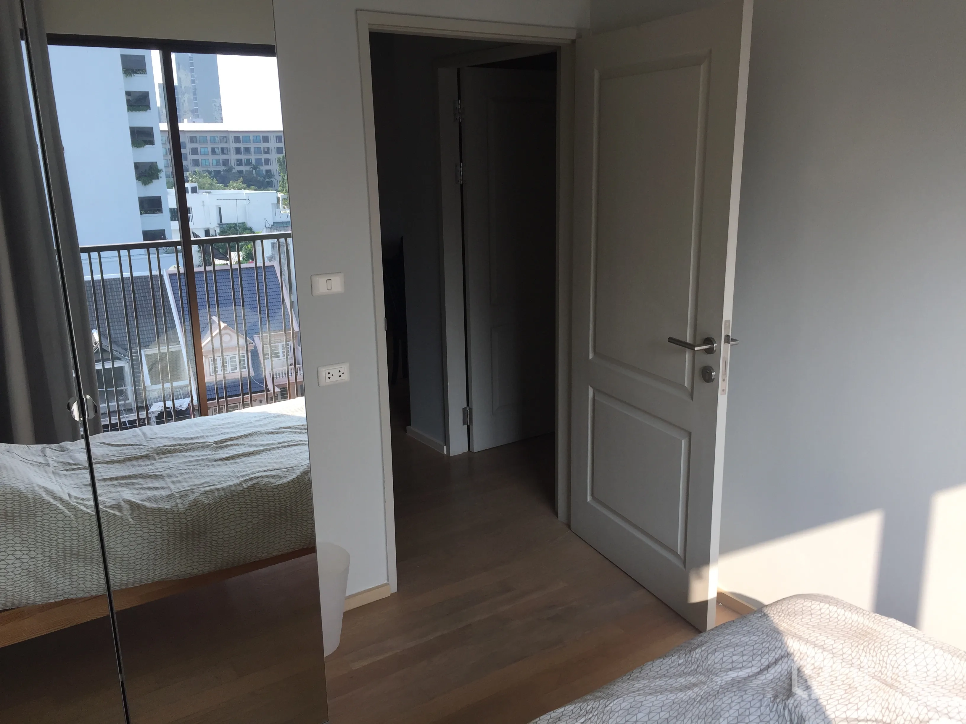 Condominium for rent in Bangkok - Bedroom with light wood floors, open door to hallway, and a large window to a balcony.