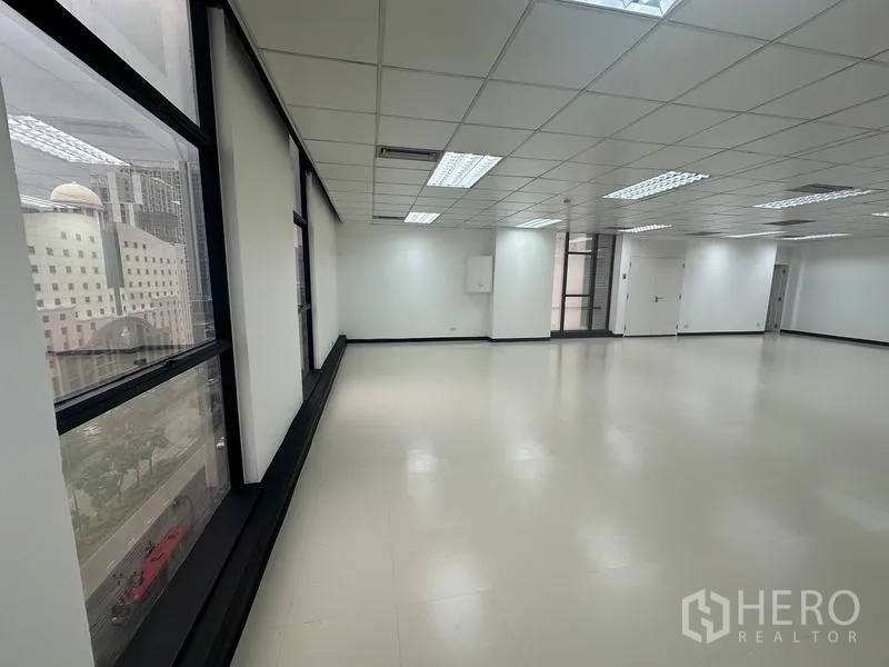 Office Space for rent - Bright open‑plan office with large windows, city views, white walls, grid ceiling and fluorescent lights.