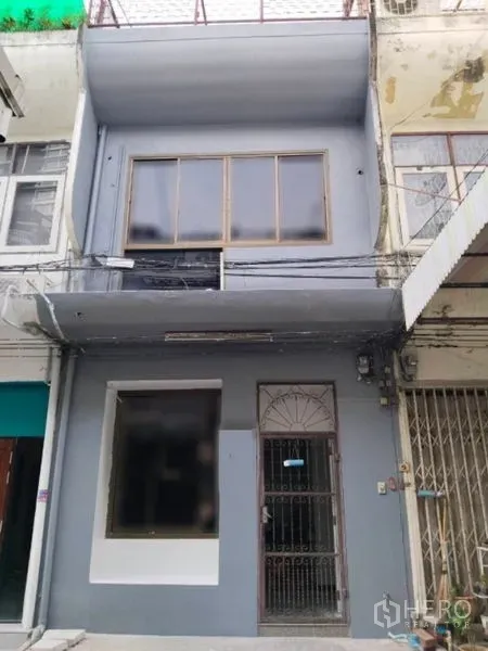 店屋 出租在Watthana, Bangkok - 两层商铺外观，宽大橱窗与金属栅栏门，位于城市排屋中。