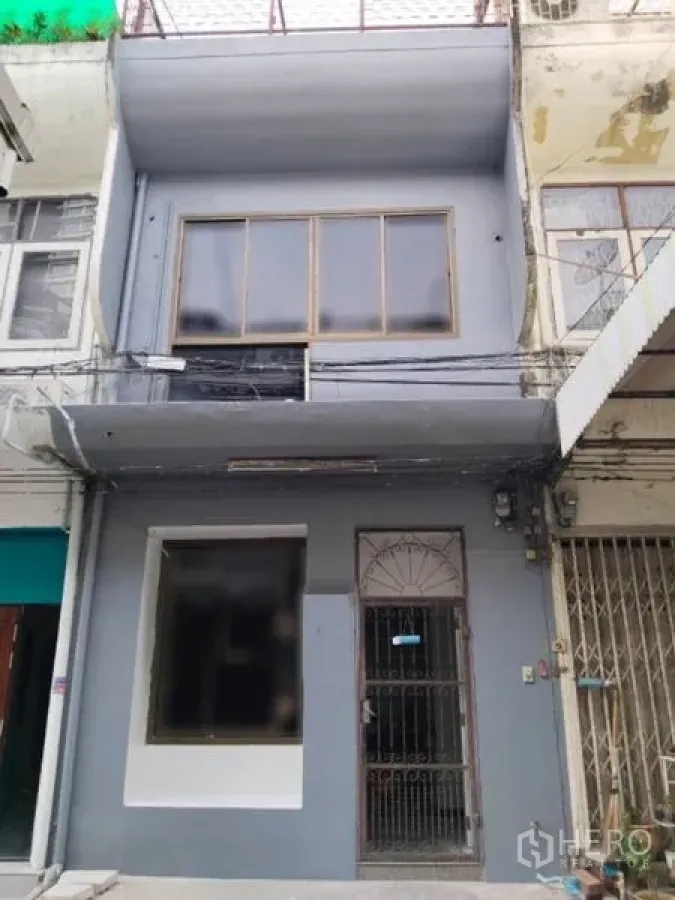 店屋 出租在Watthana, Bangkok - 两层商铺外观，宽大橱窗与金属栅栏门，位于城市排屋中。