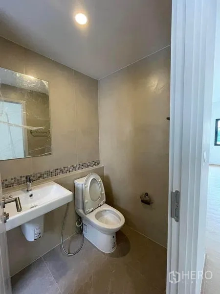 联排别墅 出租在Prawet, Bangkok - 紧凑卫浴，配坐便器、方形洗手盆、镜子与中性色瓷砖墙。