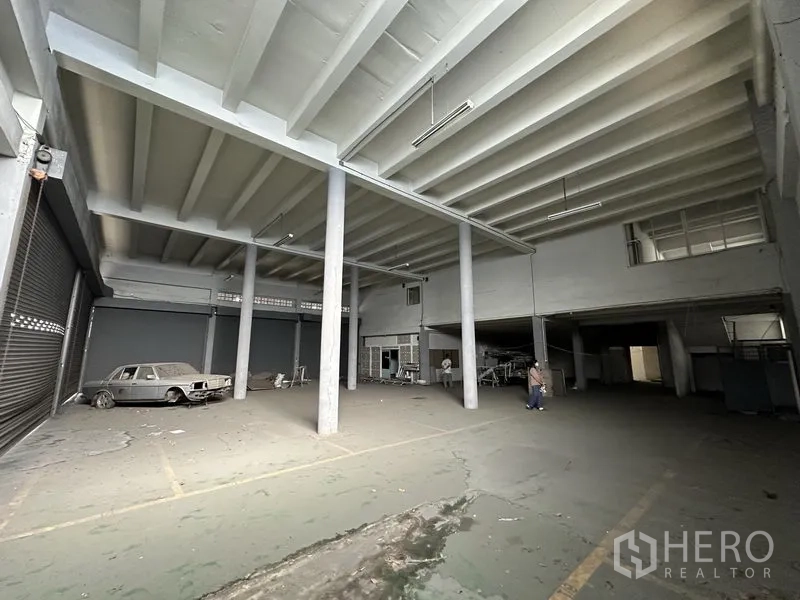 Home Office for rent in Khan Na Yao, Bangkok - High-clearance warehouse hall with concrete pillars, roller doors and a mezzanine office area.