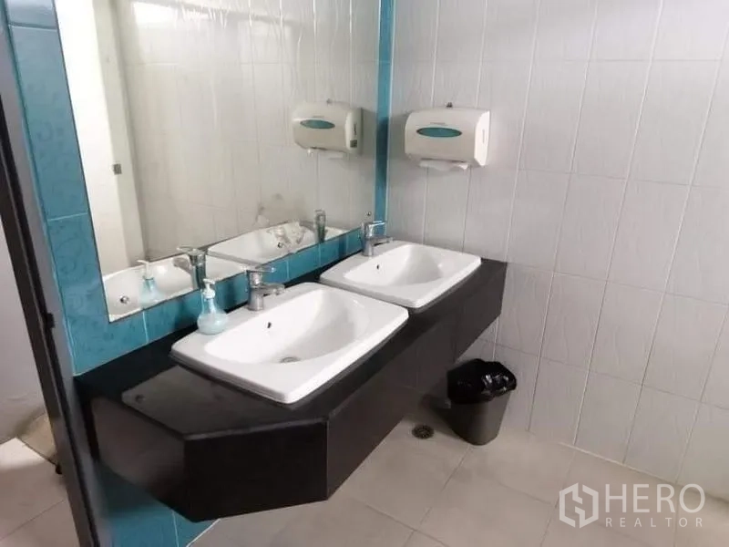 Office Space for rent - Restroom with double sinks on a black countertop, large mirror and wall-mounted dispensers.