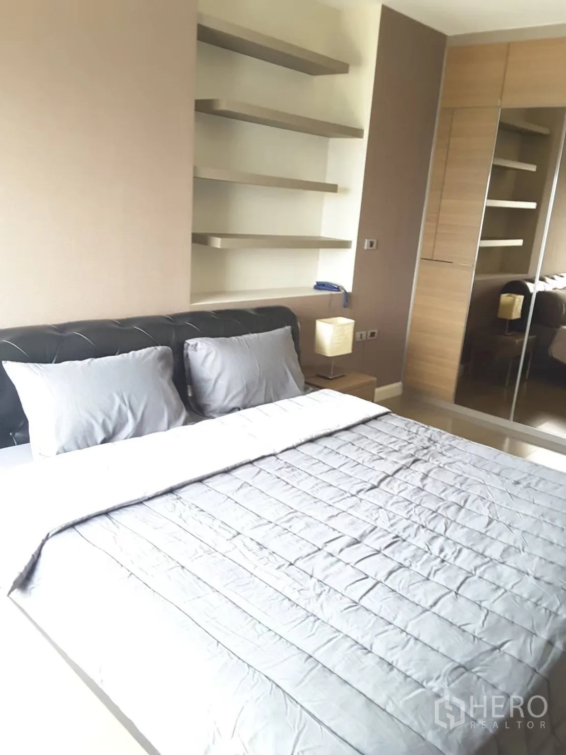 Condominium for rent in Khlong Toei, Bangkok - Bright bedroom with a queen bed, floating shelves, and a mirrored wardrobe.